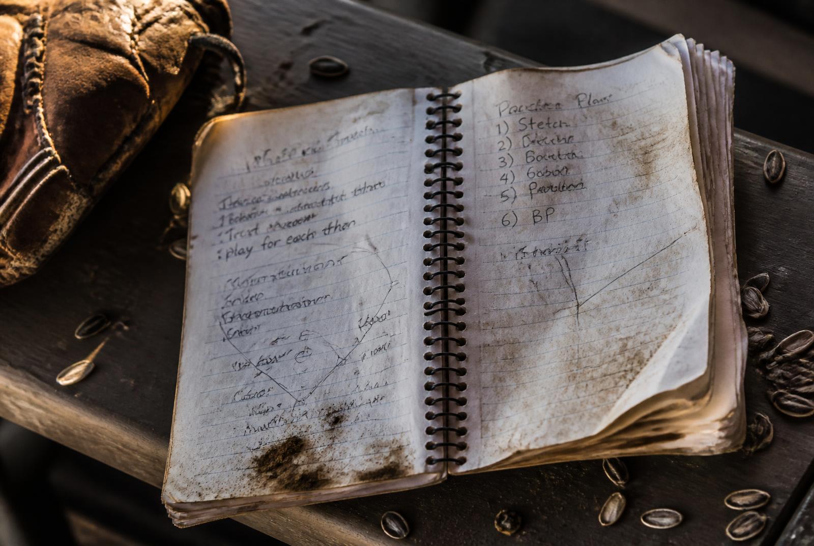 A dirty, crumpled paper baseball notebook with messy handwriting on a dugout bench